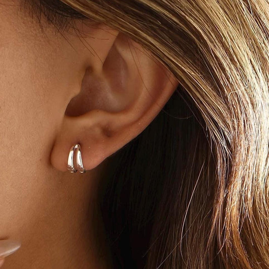 A close-up of a model wearing a everyday tiny silver hoop earring with a v shaped design