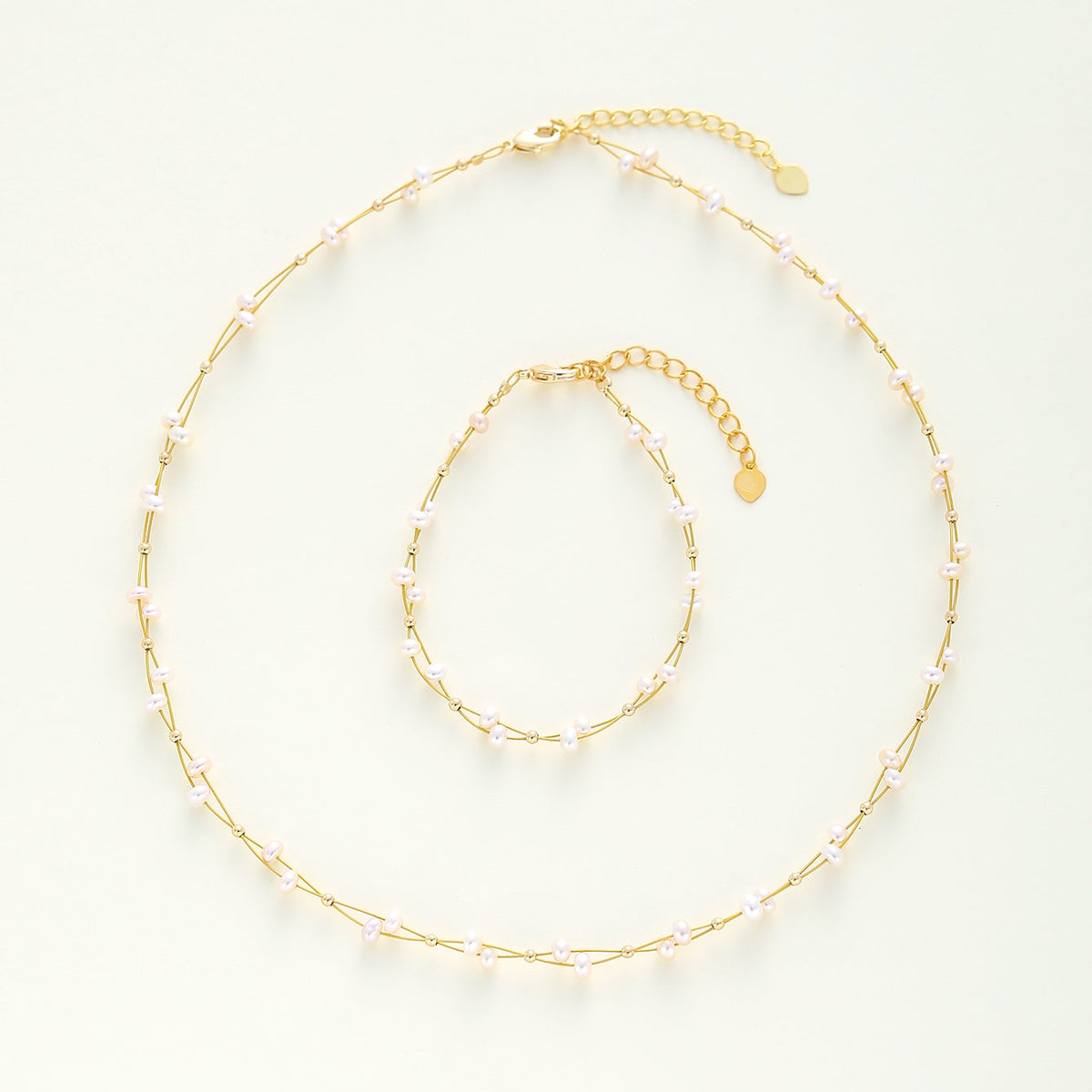 A delicate gold-toned choker necklace and matching bracelet, both adorned with small pale pink beads and chain links, displayed on a clean off-white background.