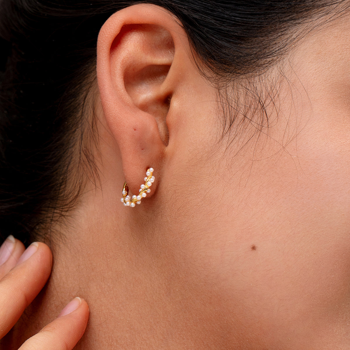 A close-up of a women ear wearing a small gold pearl hoop earring adorned with tiny white pearls.