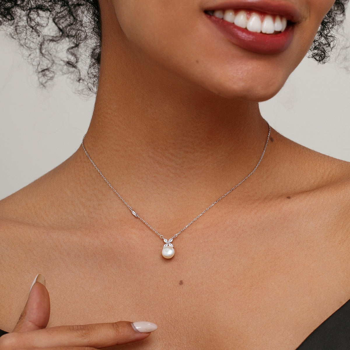 A close-up of a model wearing a minimalist silver necklace with a small white pearl pendant and a tiny flower cz