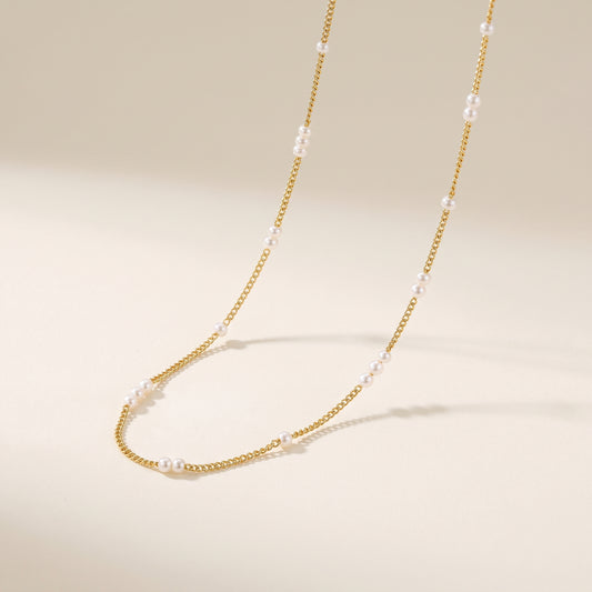 A dainty gold choker necklace adorned with 2mm white pearls, elegantly draped on a warm beige background.
