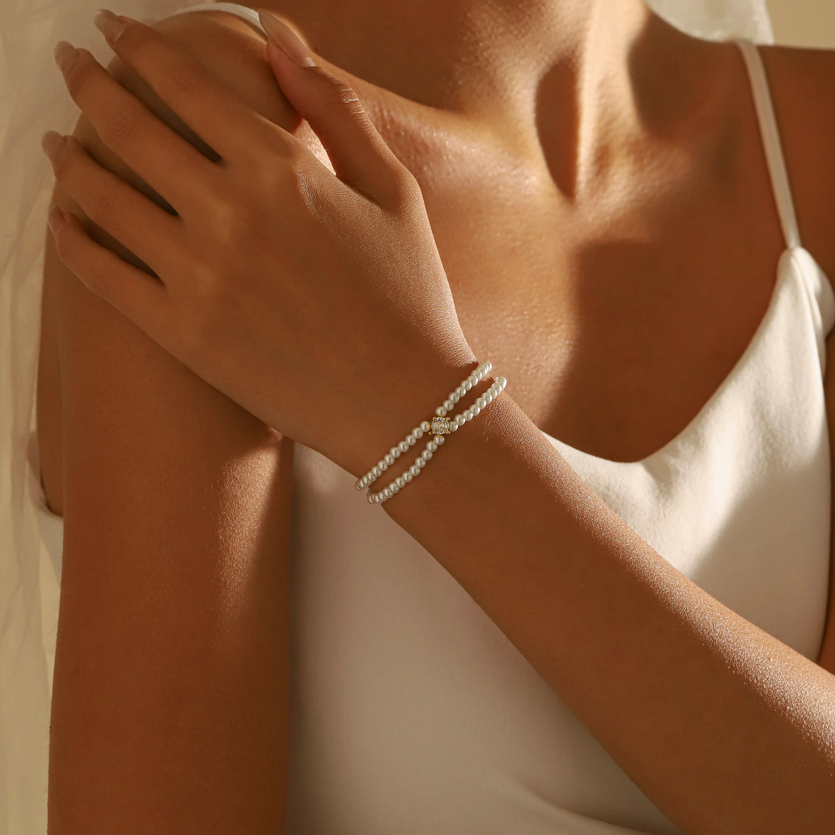 A close-up shot of a bridesmaid wearing a double layer pearl beaded bracelet with a small gold cross accent on the front, paired with a white camisole top