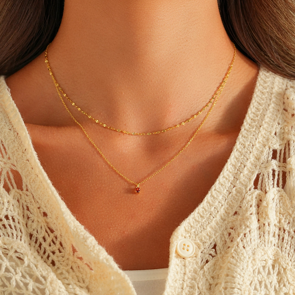 Model styled with layered gold chains and July birthstone ruby choker on v-neck top.