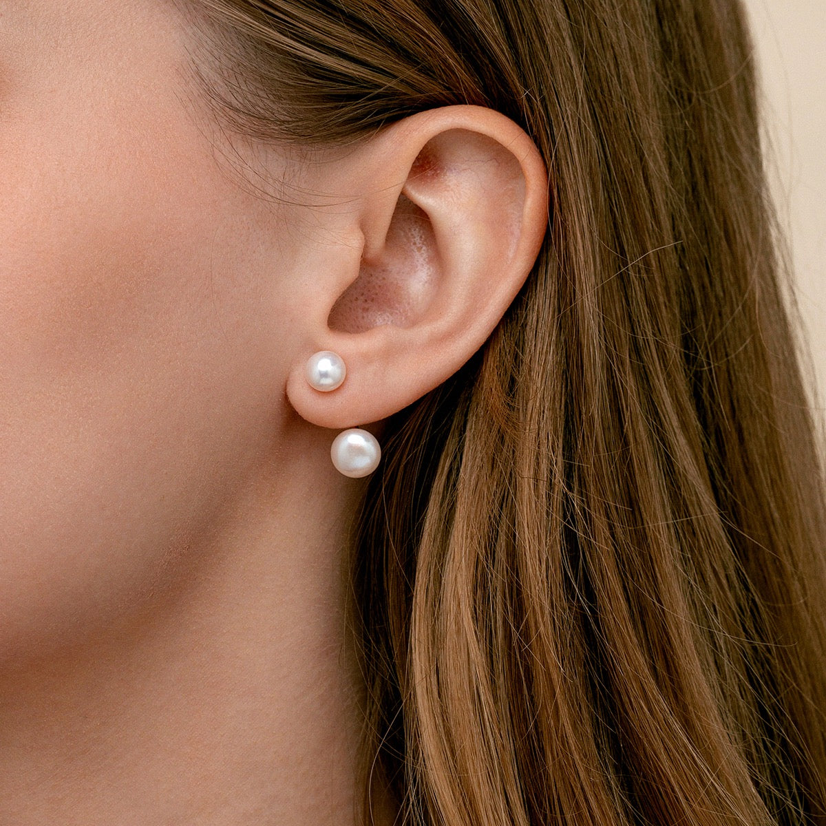 A close-up of a woman's ear wearing a pair of double pearl stud earrings which are ear jackets