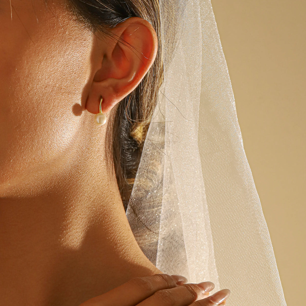 A close-up of a bridesmaid's ear wearing a dainty gold pearl earring studs