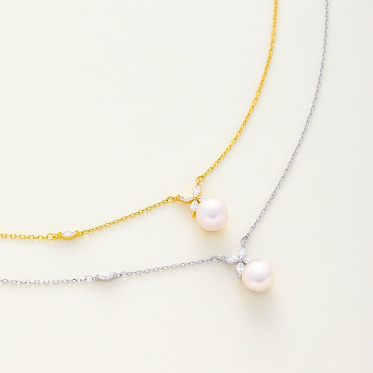 Two dainty pearl and floral cz necklace laid on a light cream background, available in gold and silver finish