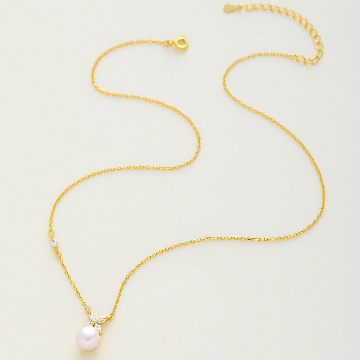 A delicate gold chain necklace featuring a single white freshwater pearl pendant, displayed on a clean, light off-white background.