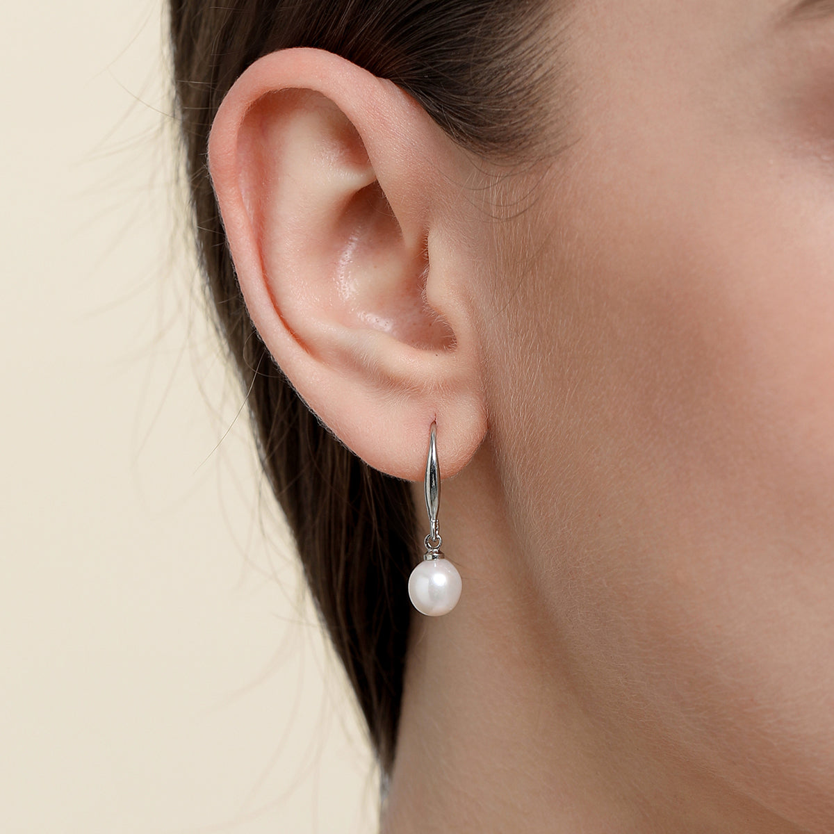 A close-up of a model's ear wearing a silver drop earring with a single white pearl.