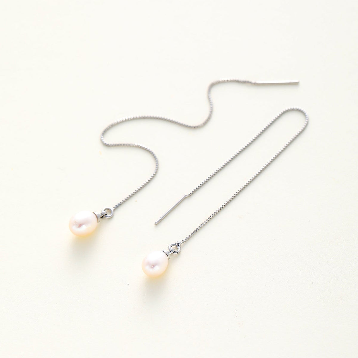 A pair of dainty long silver chain drop earrings with small white freshwater pearls hanging from the chains, displayed on a clean off-white background.