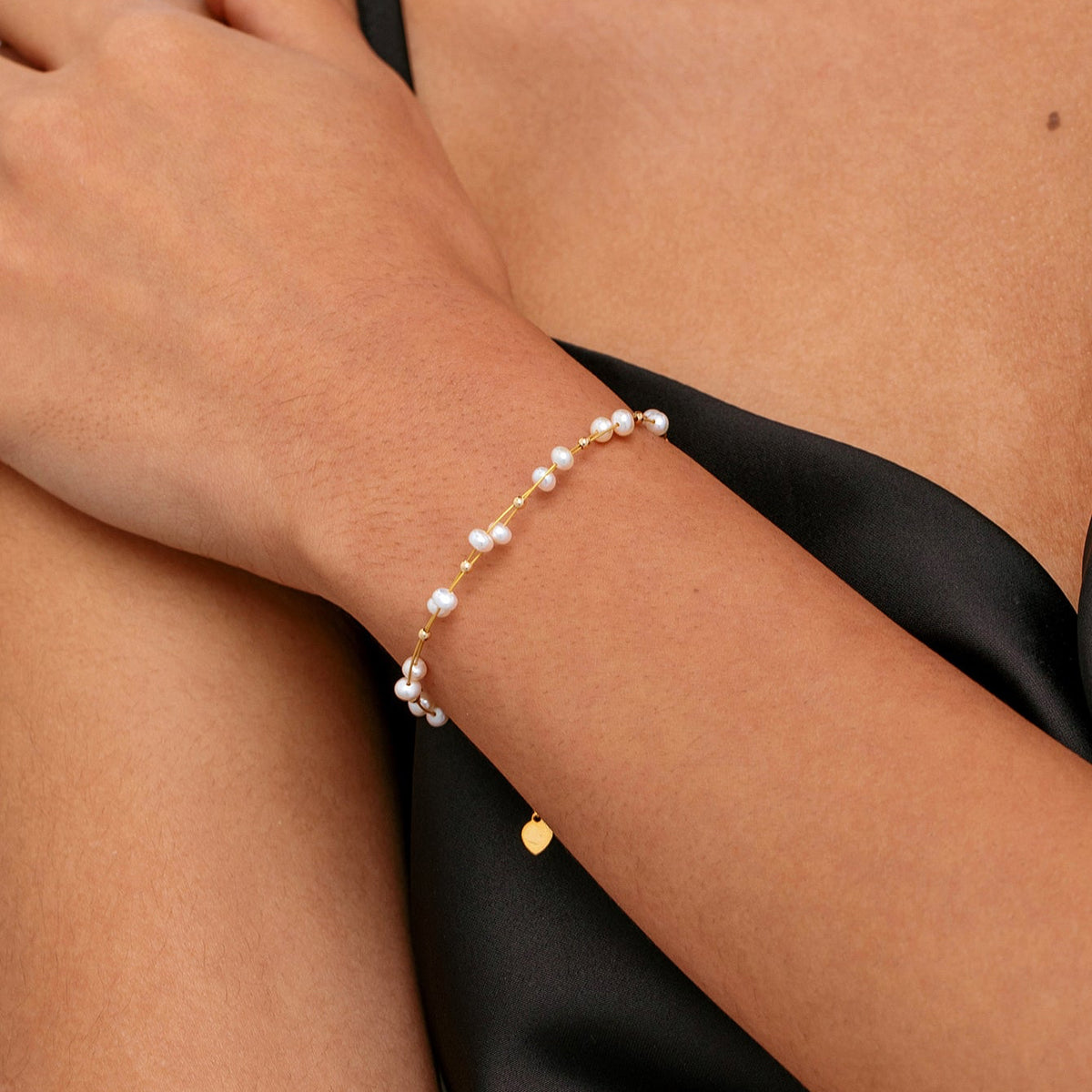 A close-up of a model's wrist wearing a delicate gold freshwater pearl bracelet with adjustable extension chain