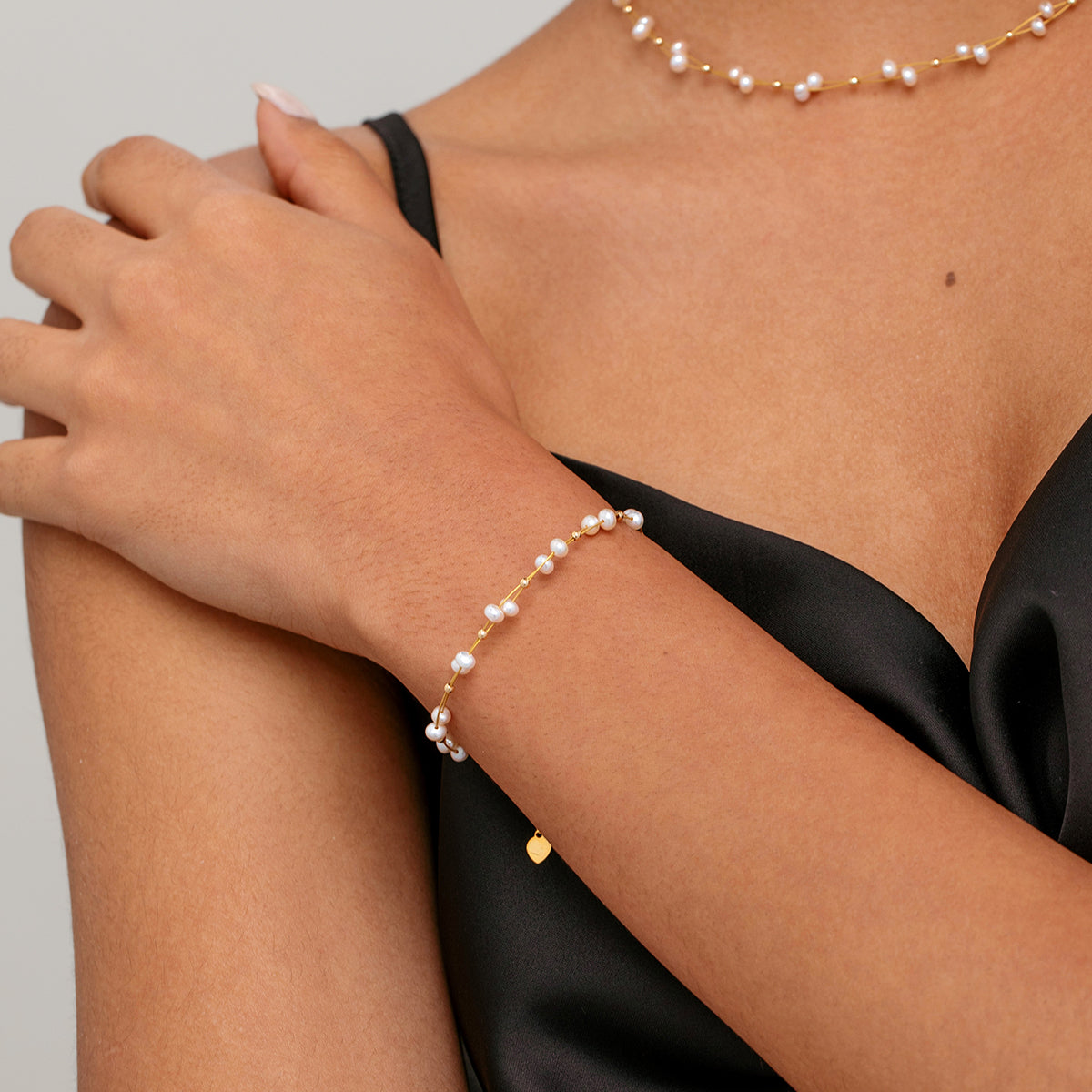 A close-up of a model's wrist wearing a delicate gold bracelet tiny white pearls and extender chain with a matching necklace 