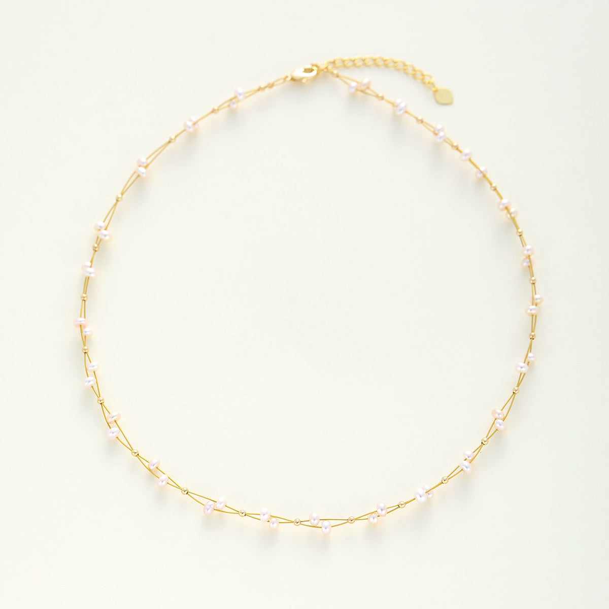A wedding gold necklace with small, evenly spaced dainty pearls, displayed on a clean, light off-white background.