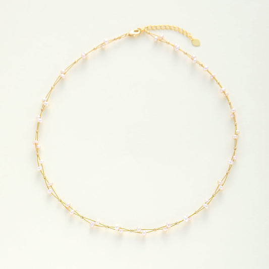 A wedding gold necklace with small, evenly spaced dainty pearls, displayed on a clean, light off-white background.