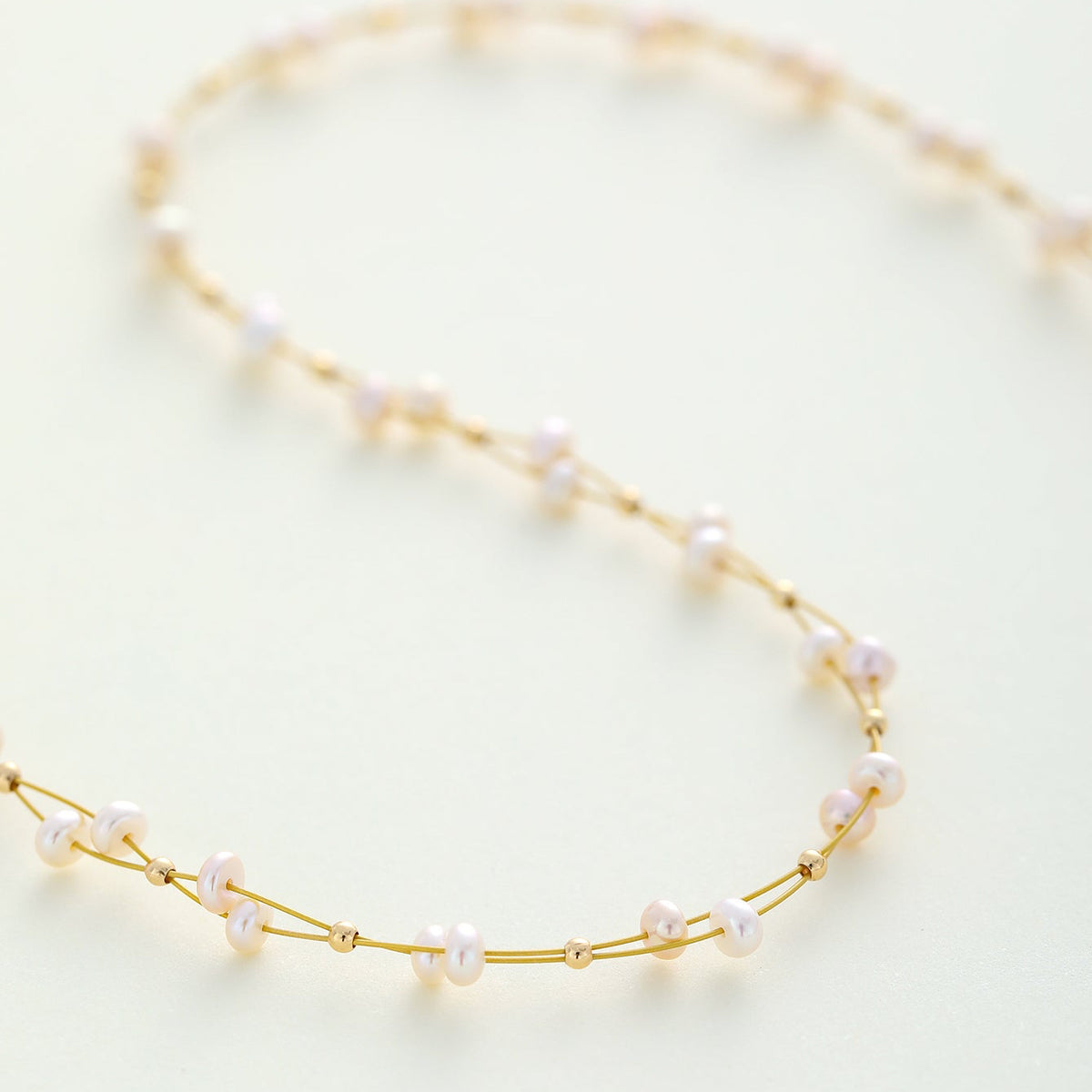 A delicate bridal gold freshwater pearl wreath necklace arranged in a soft loop on a light cream background.