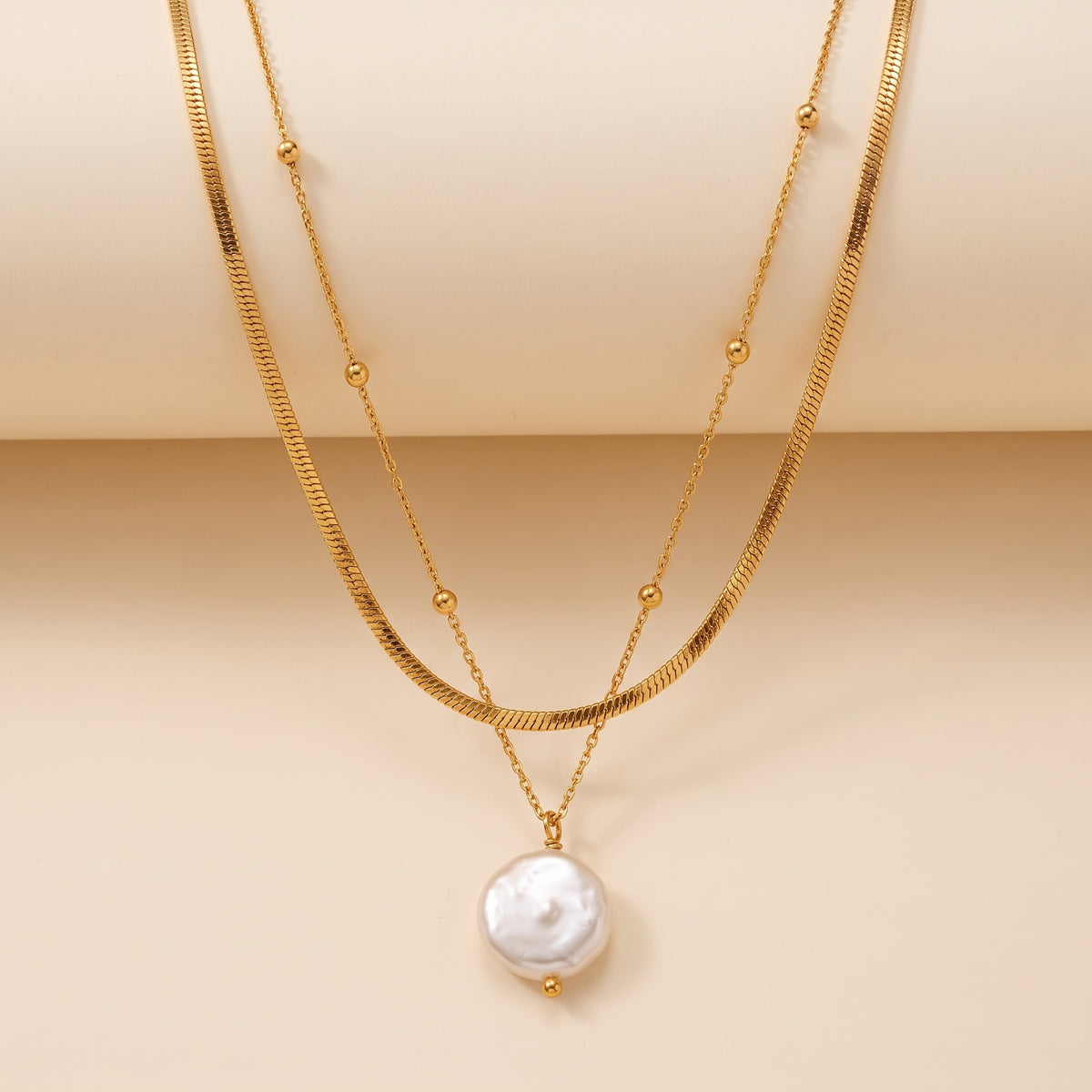 A double layered gold necklace featuring a textured snake chain and a irregular white baroque pearl