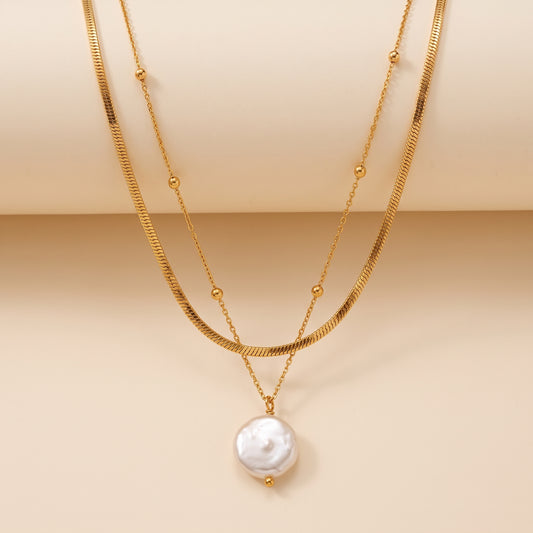 A double layered gold necklace featuring a textured snake chain and a irregular white baroque pearl