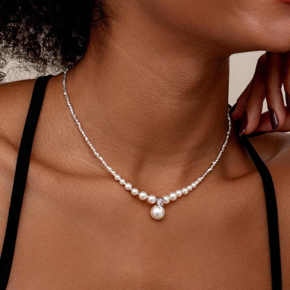 A close-up of a model wearing a delicate wedding silver chain necklace with a row of small white pearls and a larger central pearl pendant.