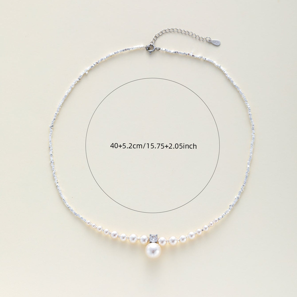A silver-toned choker necklace with a central white pearl and a small clear rhinestone, displayed on a light beige background with a measurement circle and text reading 40+5.2cm/15.