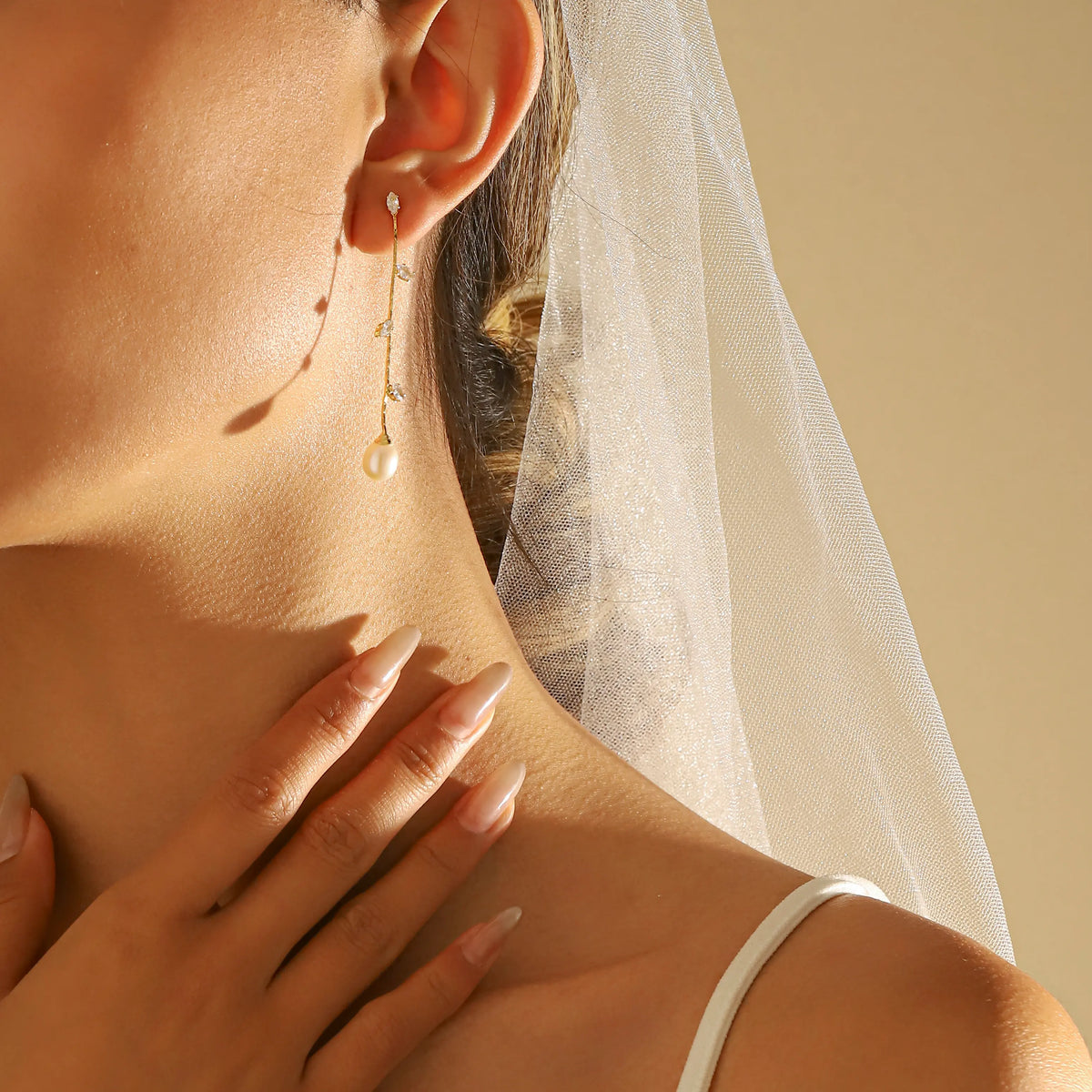 A close-up lifestyle shot of bride wearing a wedding long dangle gold earring with a small pearl and tiny gold leaves, styled with a white bridal veil