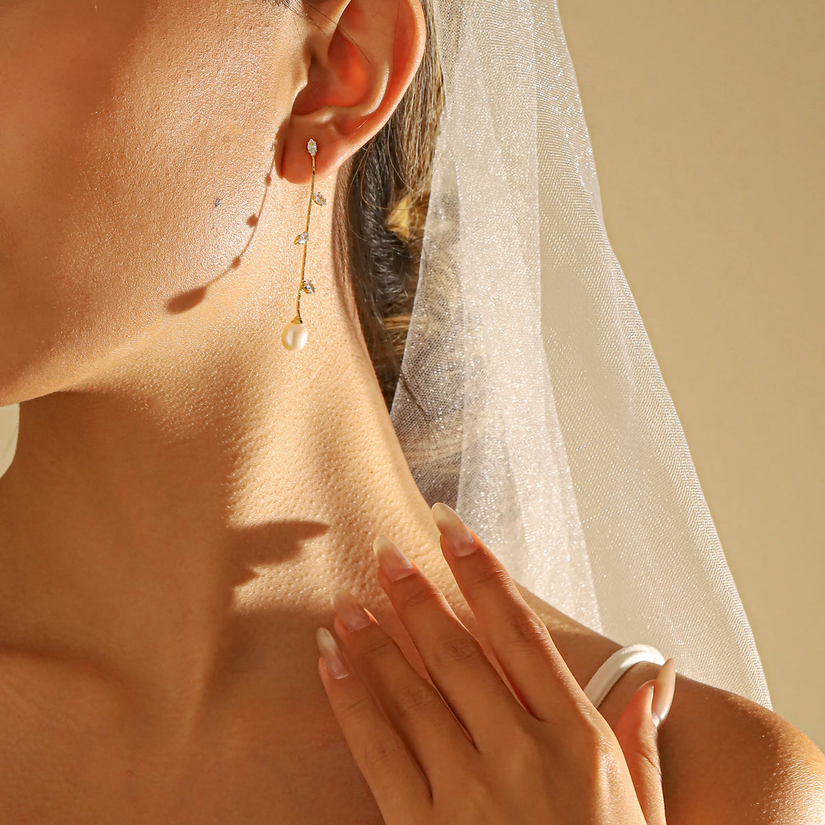 A close-up of a bride wearing a statement gold long drop earring with a single pearl, a white bridal veil