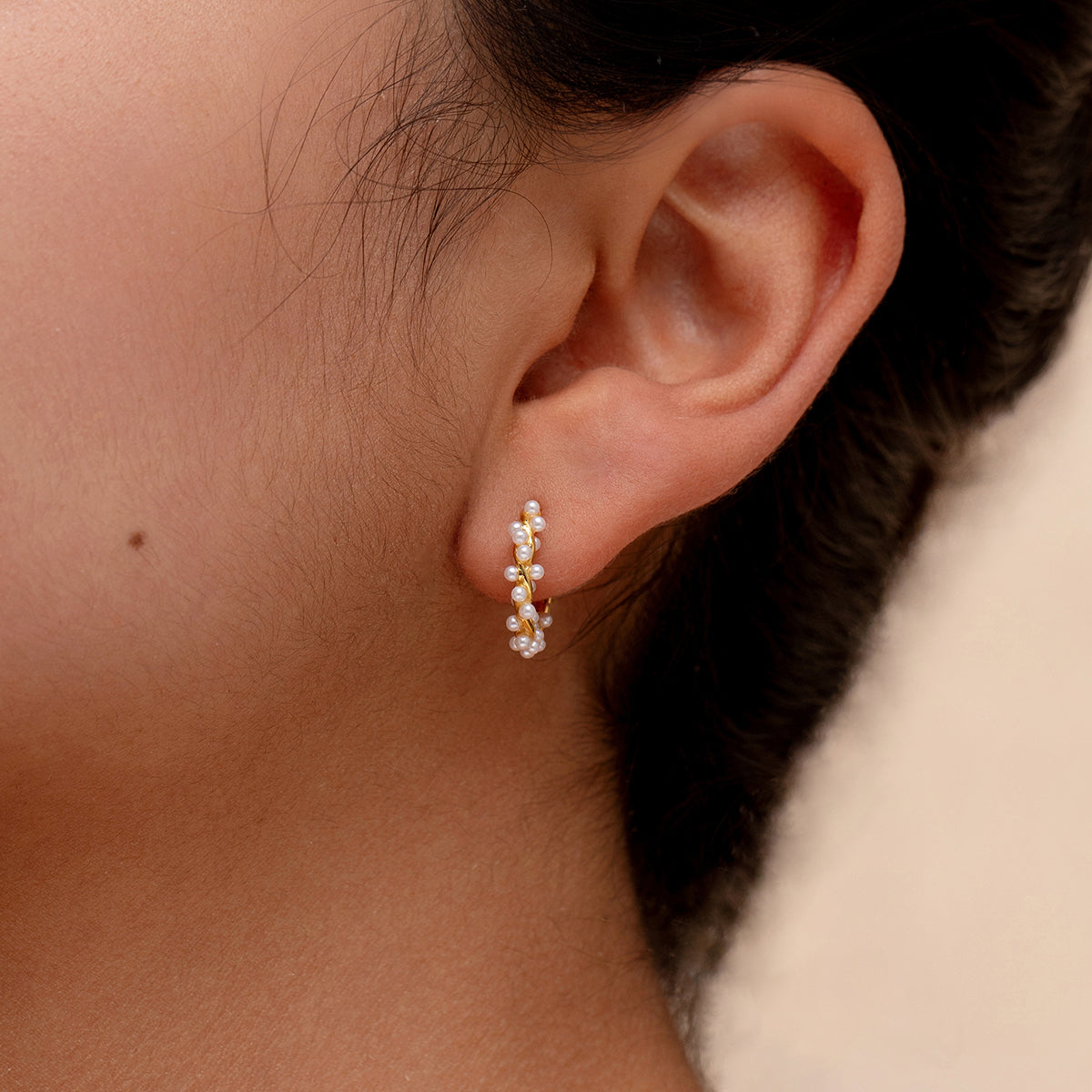 A close-up of a person's ear wearing a gold hoop earring with tiny pearls