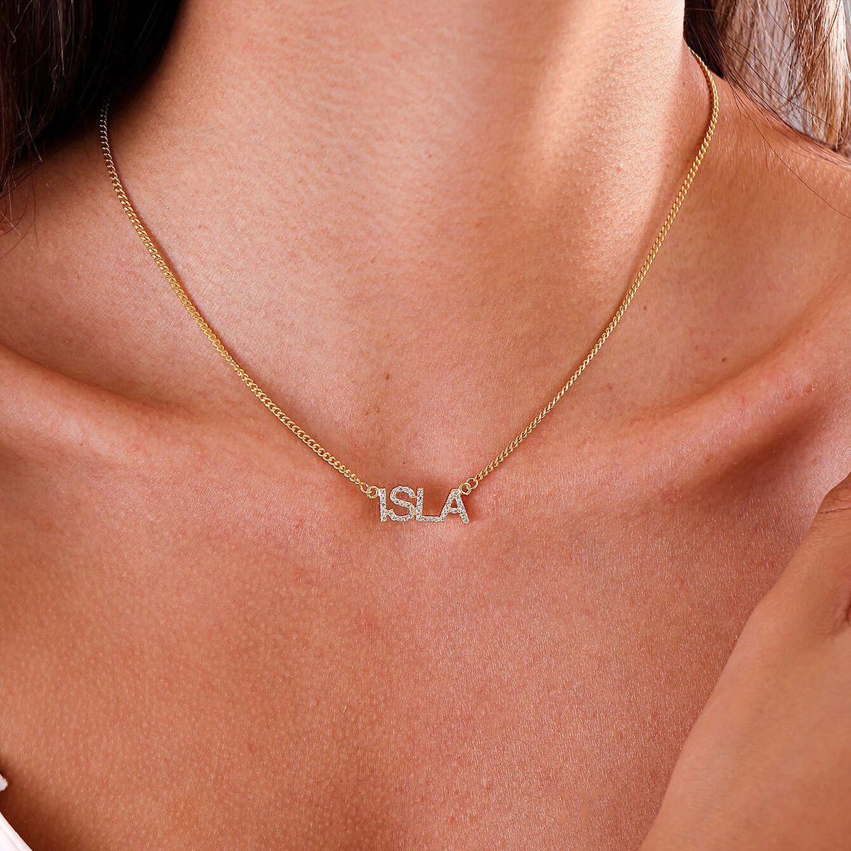 A close-up of a model wearing a delicate gold chain necklace with a small silver custom name pendant.
