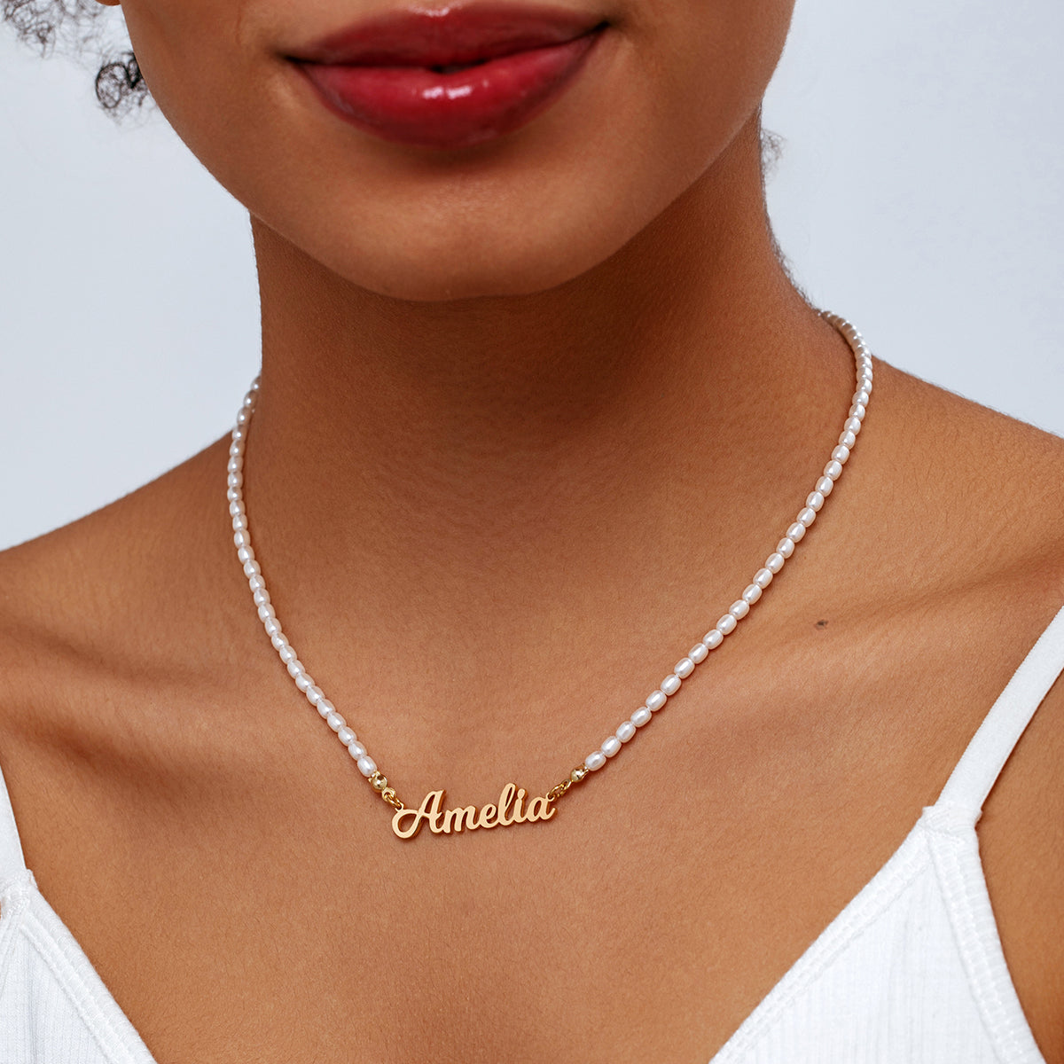 A close-up of a model wearing a personalised white pearl necklace with a gold custom nameplate
