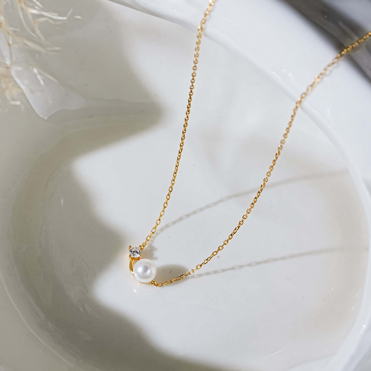 A gold necklace with a dainty single white pearl pendant and a cz stone