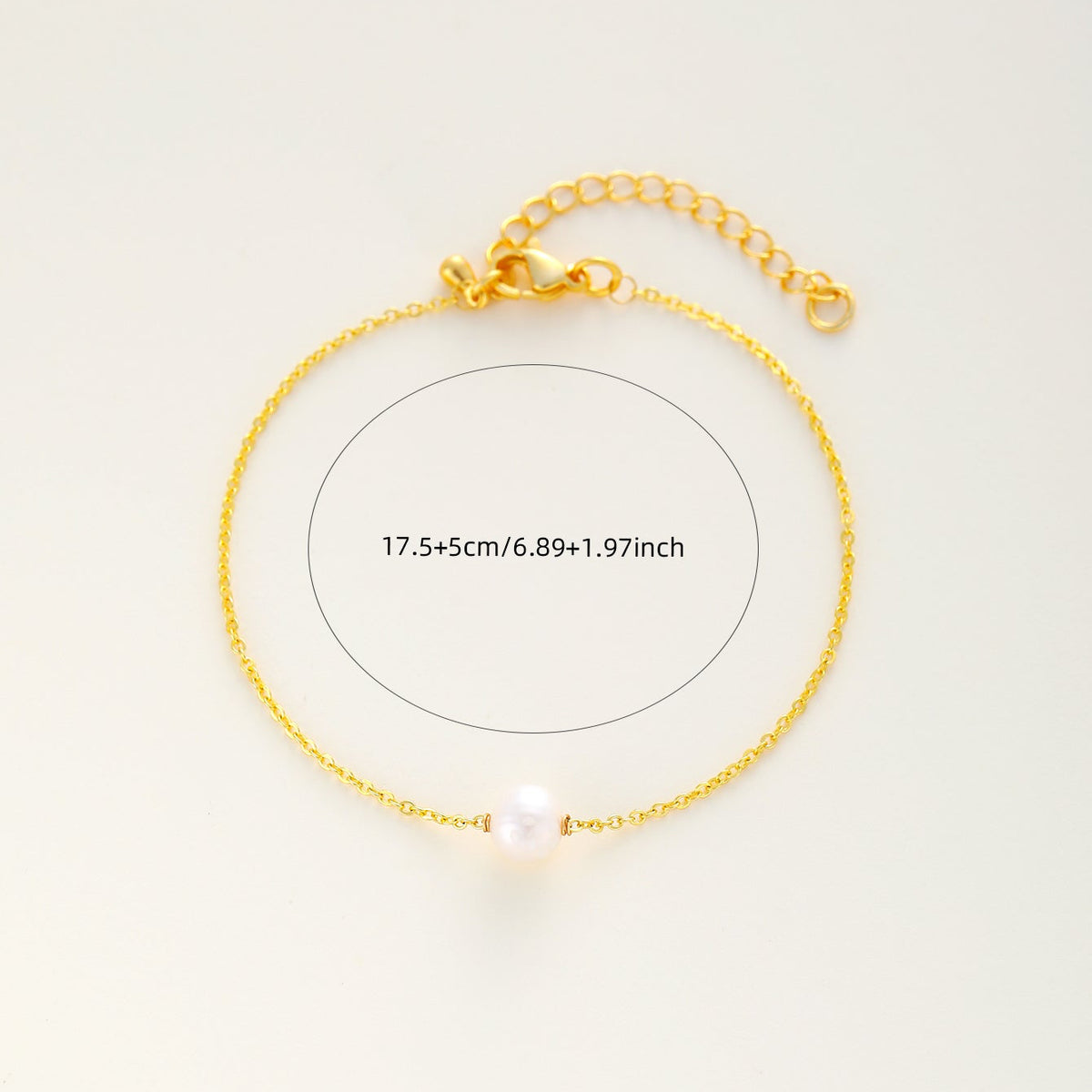 A delicate gold chain bracelet with a single white pearl bead, displayed on a clean off-white background with a measurement overlay circle and text indicating its length.