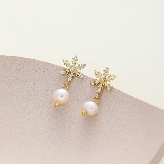 A pair of gold snowflake dangle earrings with cz and a single white pearl drop
