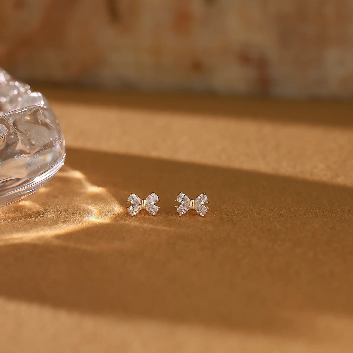 Elegant gold bow studs placed on soft linen fabric, representing quiet luxury everyday jewelry.