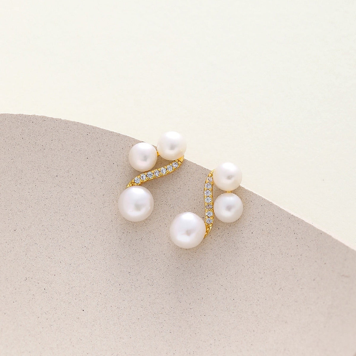 A pair of gold-plated triple freshwater pearls earrings displayed on a neutral beige surface.