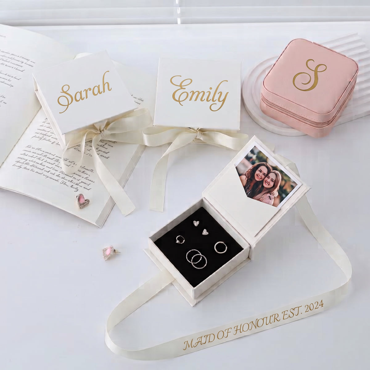 Personalized jewelry gift boxes with white lids, gold script names, cream ribbons, and a photo insert, arranged on a white surface with rings displayed in one open box.